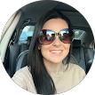 A woman with long dark hair and large sunglasses smiles while sitting in a car. Sunlight is coming through the car windows, and the background is slightly blurred. A woman with long dark hair and large sunglasses smiles while sitting in a car. Sunlight is coming through the car windows, and the background is slightly blurred.
