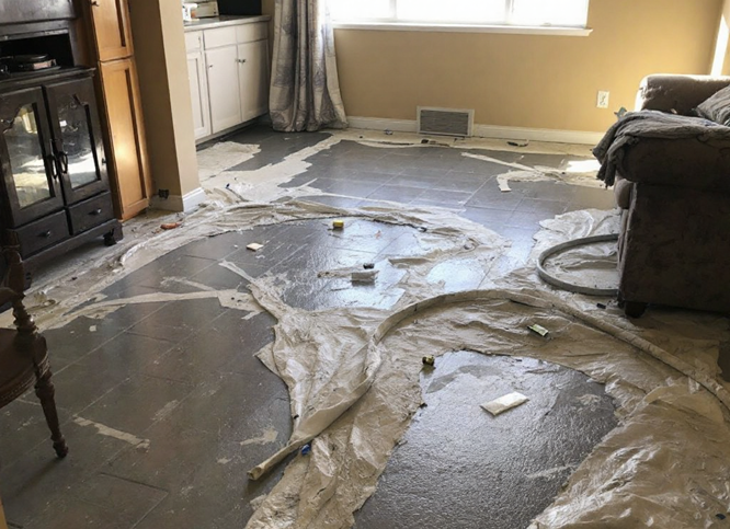 The room is in disarray, with the floor strewn in torn white plastic and debris. Amidst a wooden cabinet, a small refrigerator, and a couch by the window, signs of water damage are evident. This space clearly needs urgent water damage cleanup to restore order and peace.